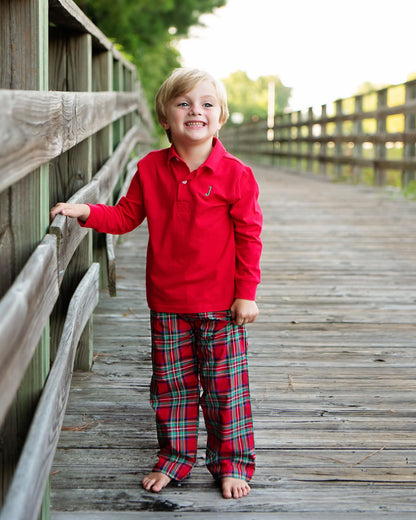 Child wearing a red shirt and plaid pants standing on a wooden bridge