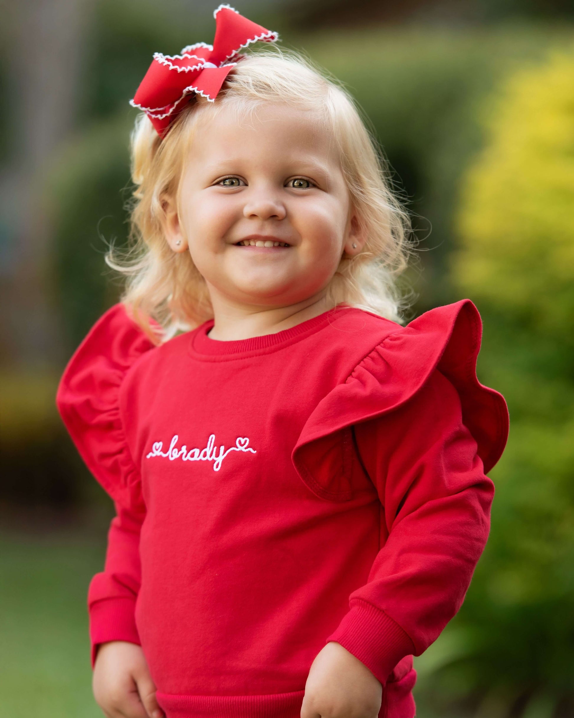 Child wearing a red shirt with a bow in her hair outdoors