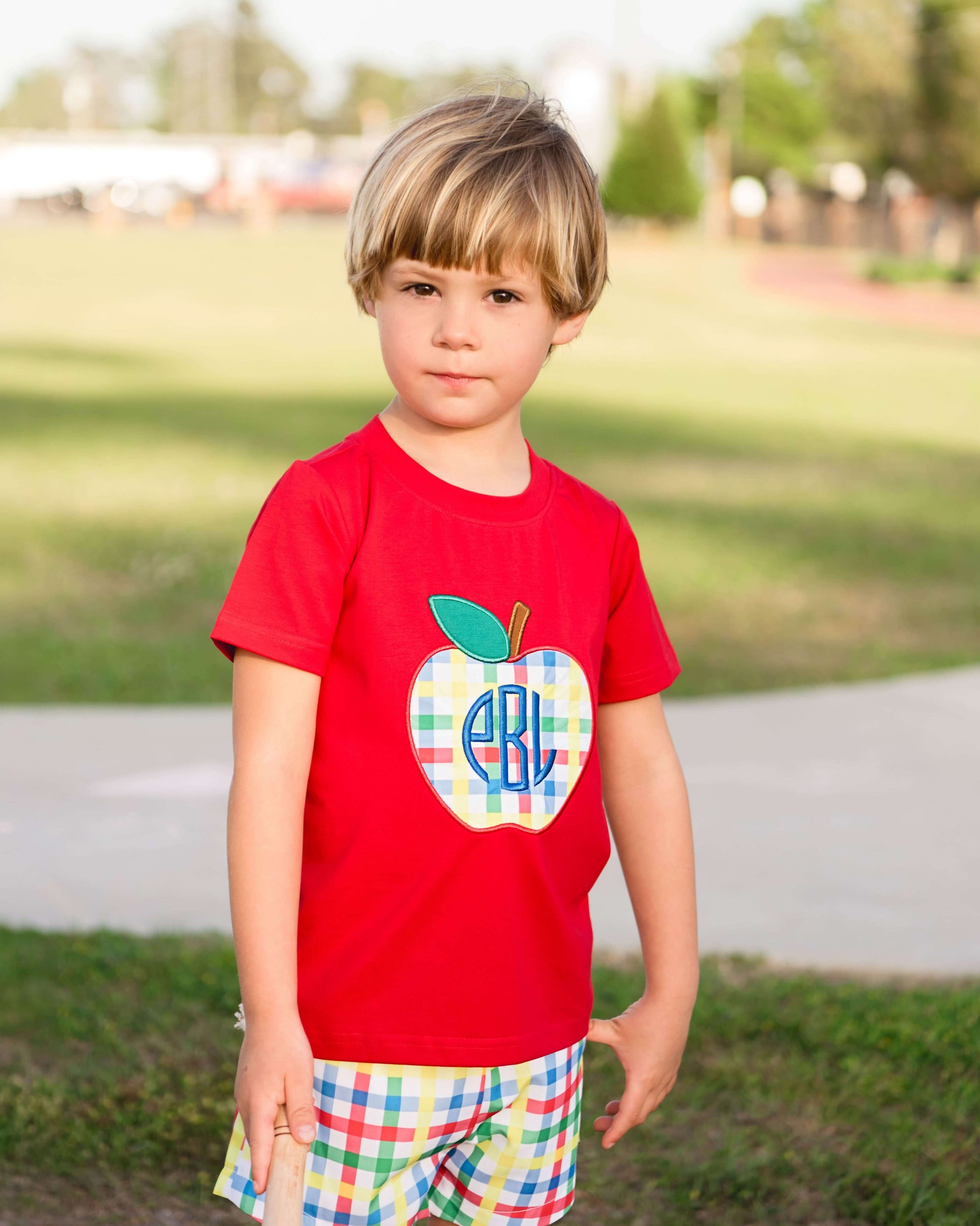Child wearing a red t-shirt with a colorful apple design outdoors.