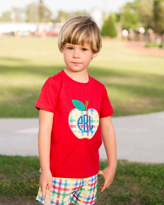 Child wearing a red t-shirt with a colorful apple design outdoors.