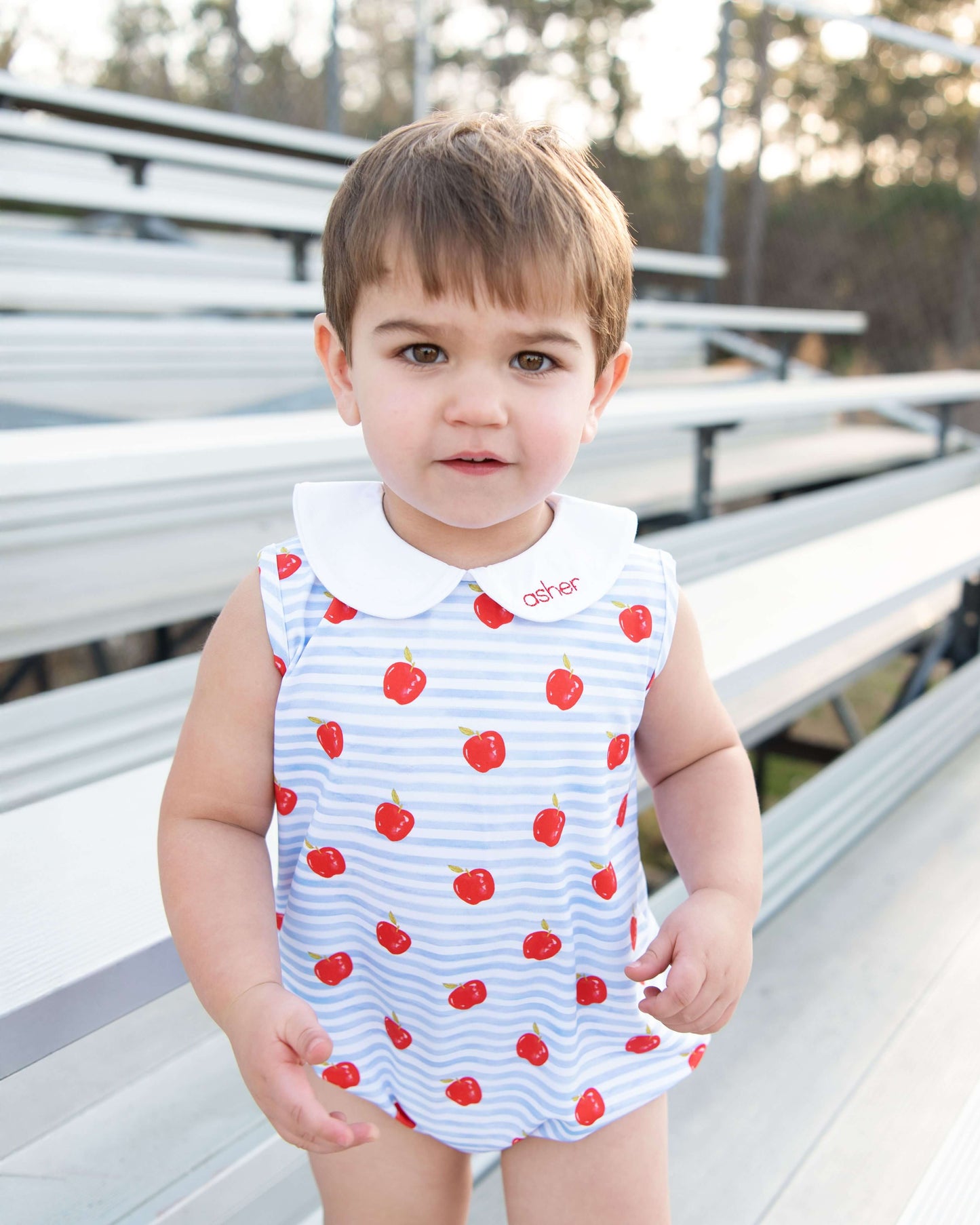 Child wearing a sleeveless bubble with red apple pattern outdoors