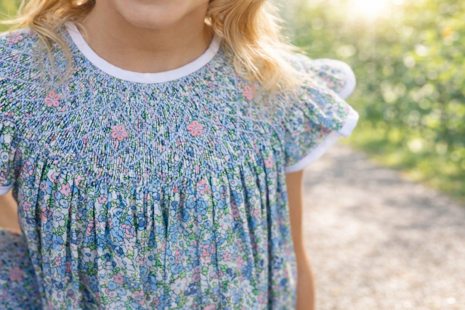 Child wearing a smocked floral dress with a blurred natural background