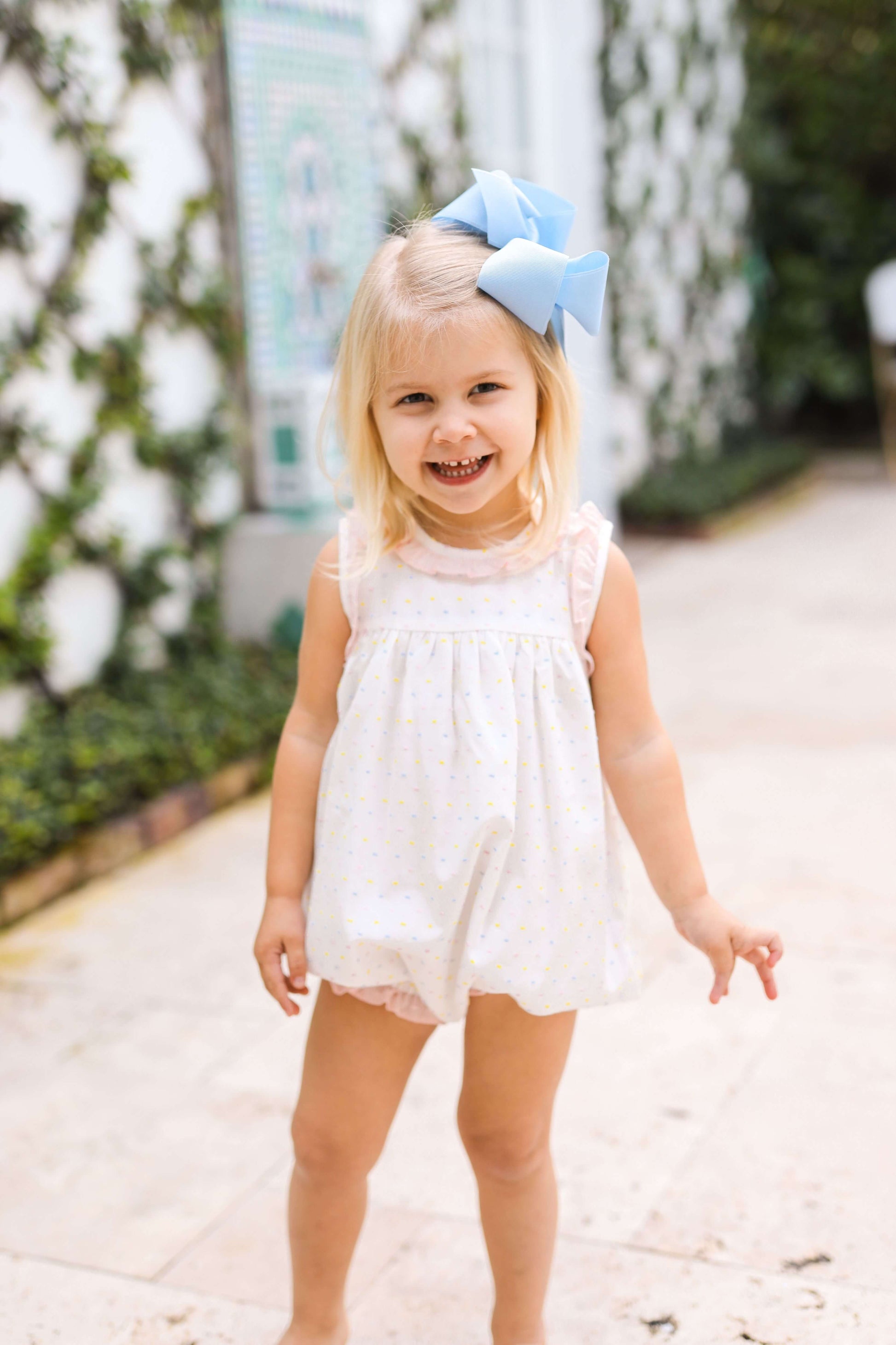 Child wearing a white dress and blue bow in an outdoor setting