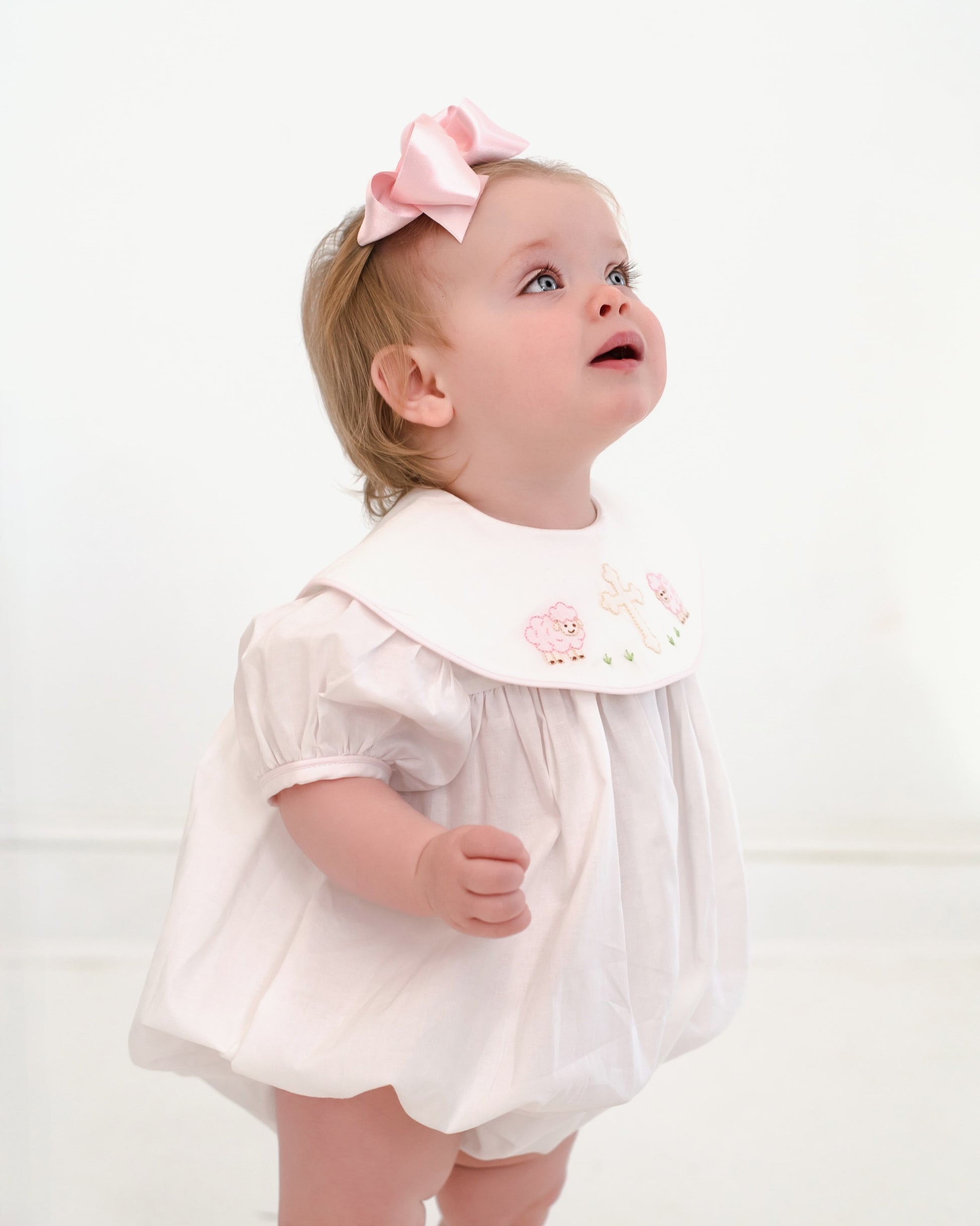 Child wearing a white dress with a pink bow on a white background