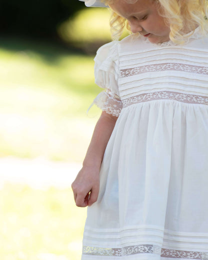 Child wearing a white dress with lace details in an outdoor setting