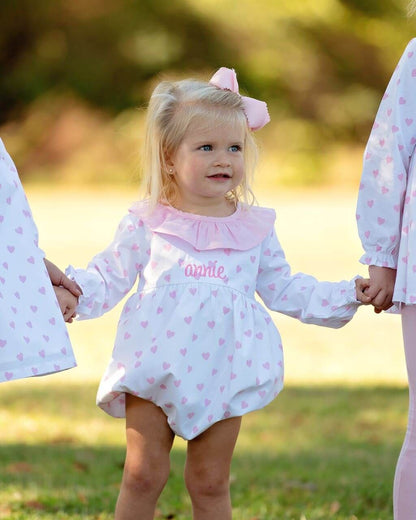 Child wearing a white dress with pink hearts and a pink bow in a park setting