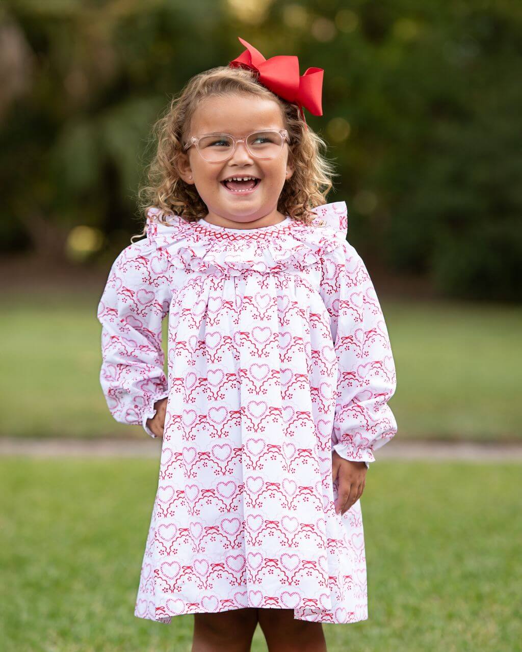Child wearing a white dress with red heart patterns outdoors