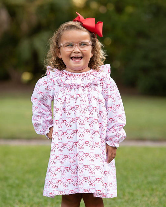 Child wearing a white dress with red heart patterns outdoors