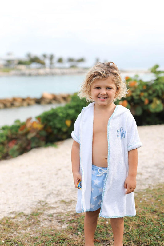 Child wearing a white hooded towel with 'SM' initials, standing by a waterfront.