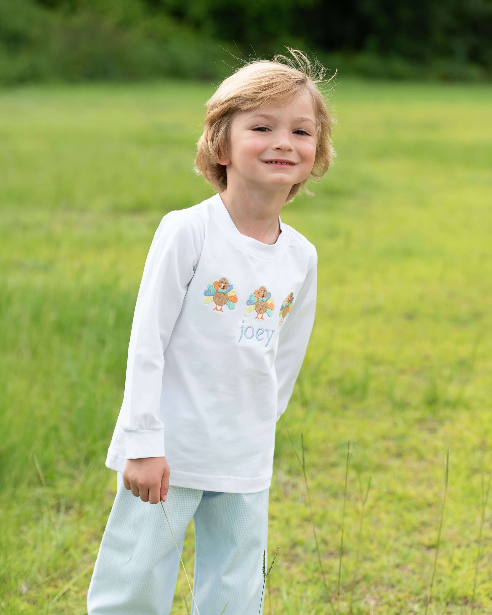 Child wearing a white long-sleeve shirt with a colorful design and text, standing in a grassy field.