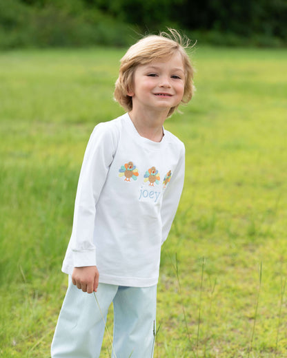 Child wearing a white long-sleeve shirt with a colorful design and text, standing in a grassy field.