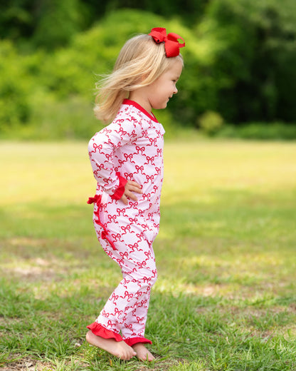 Child wearing a white outfit with red bows and trim outdoors on grass
