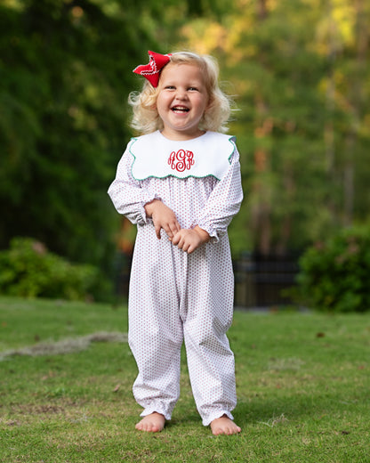 Child wearing a white patterned outfit with a red bow outdoors