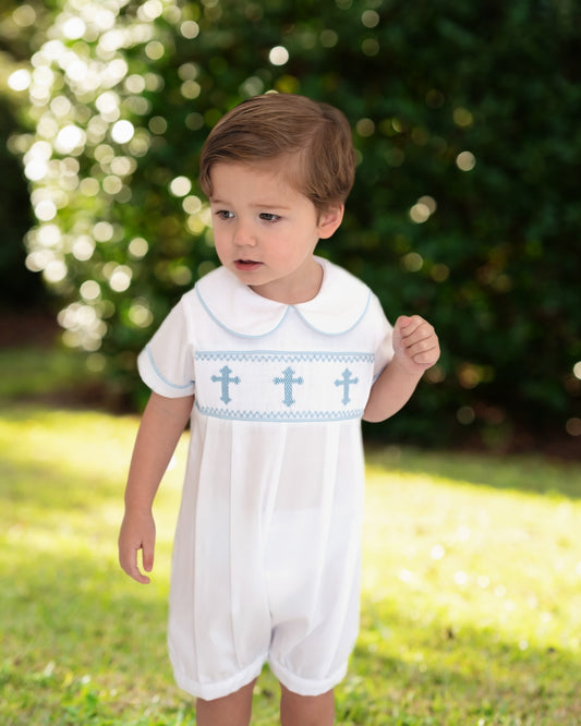 Child wearing a white romper with blue cross patterns outdoors.