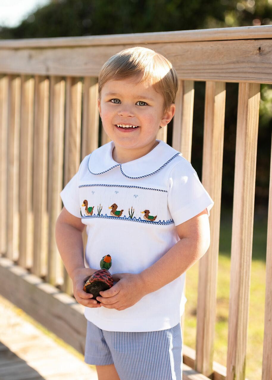 Child wearing a white shirt with a duck design outdoors on a wooden deck.