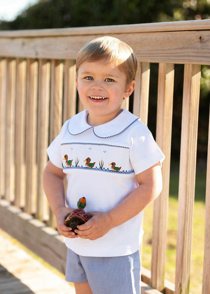 Child wearing a white shirt with a duck design outdoors on a wooden deck.