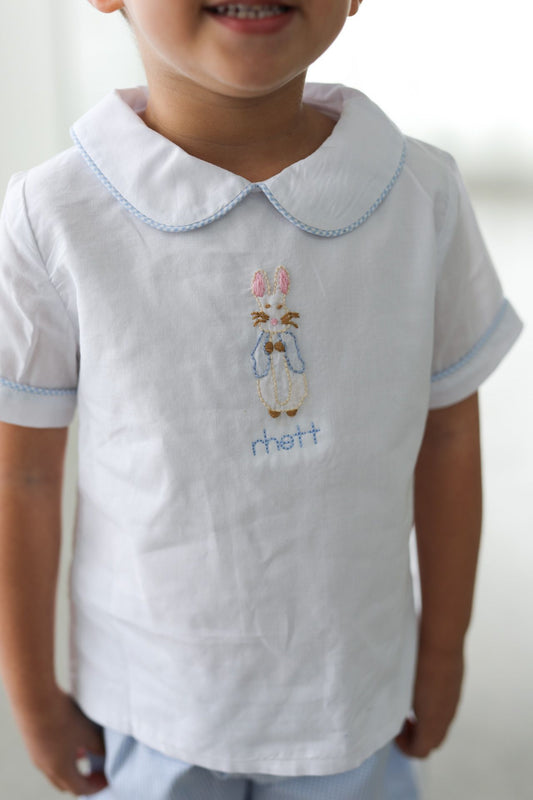 Child wearing a white shirt with embroidered bunny and name on a plain background