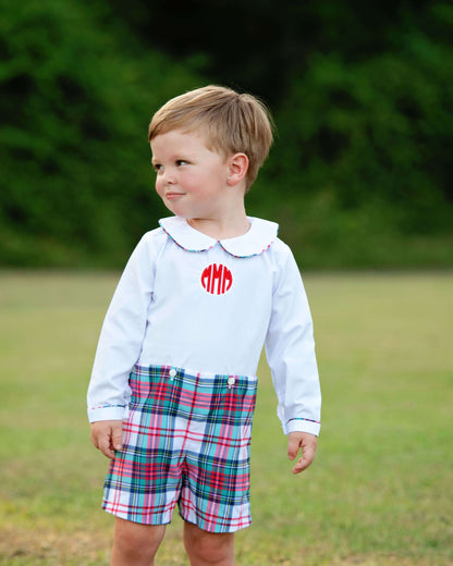 Child wearing a white shirt with red monogram and button-on plaid shorts outdoors