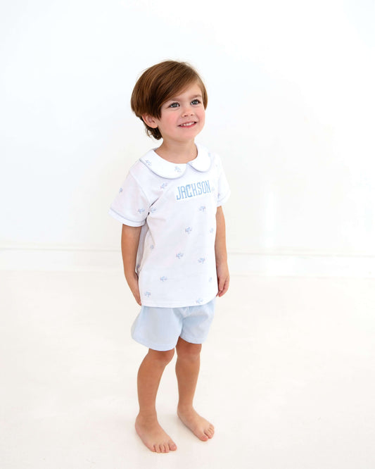 Child wearing a white shirt with text and light blue shorts on a white background