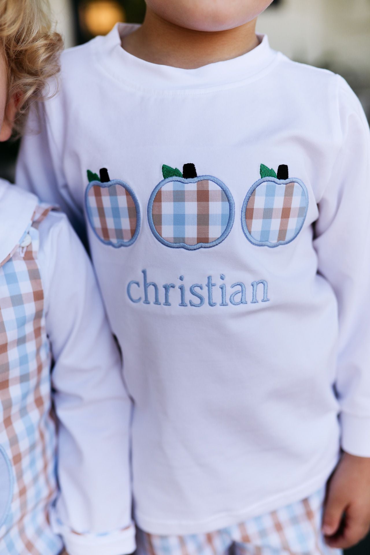 Child wearing a white sweatshirt with plaid apples and 'Christian' text.