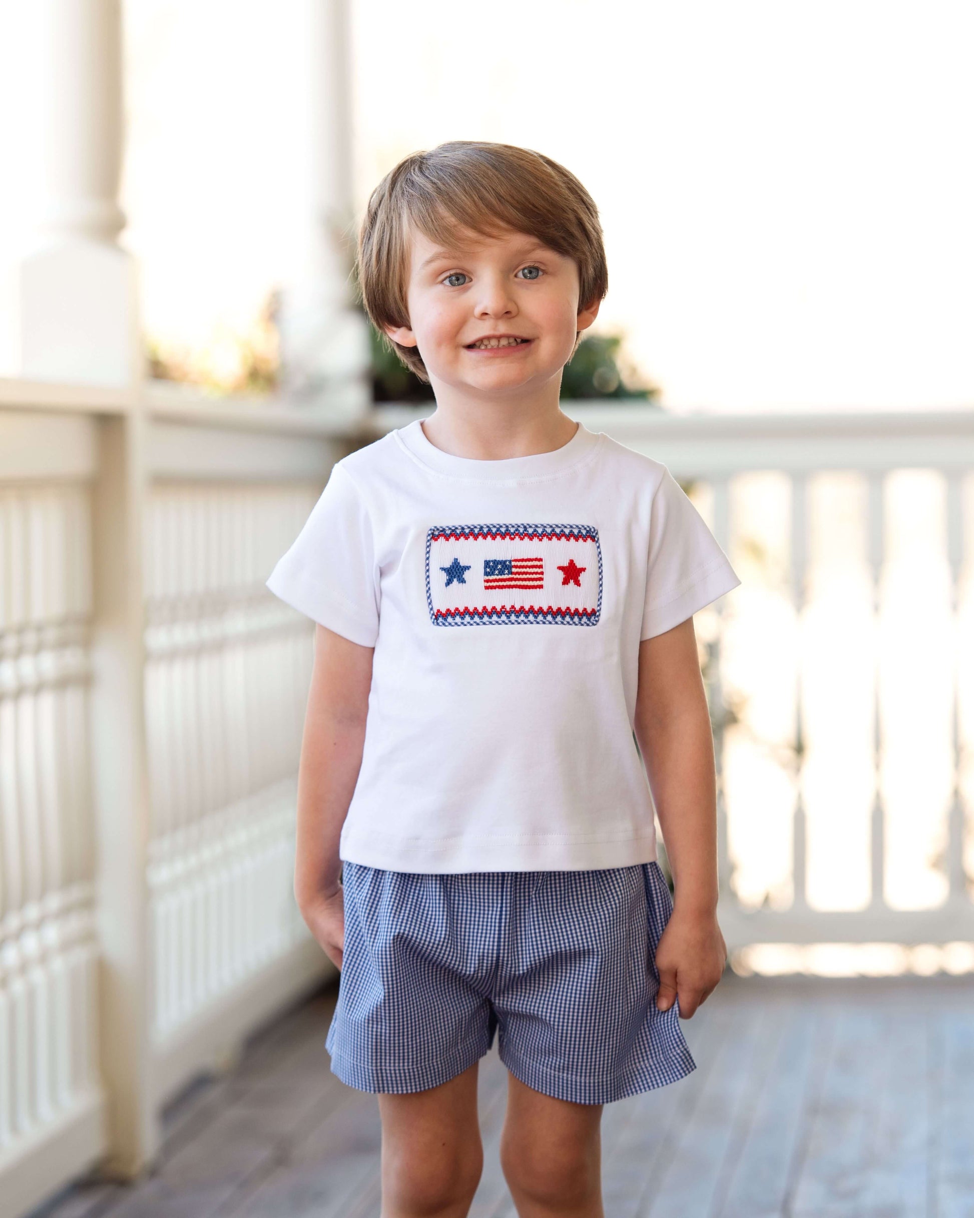 Child wearing a white t-shirt with a graphic design and blue shorts on a wooden floor.