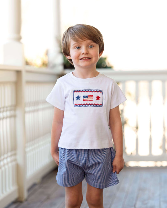 Child wearing a white t-shirt with a graphic design and blue shorts on a wooden floor.