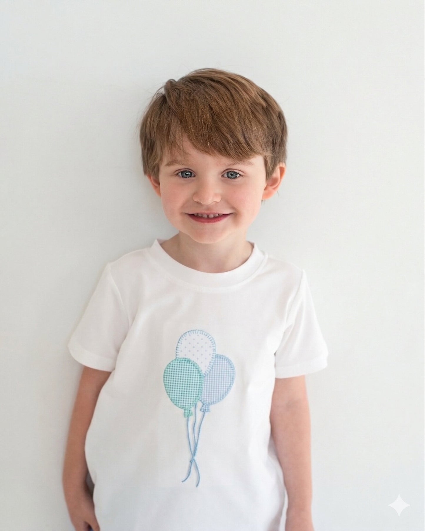 Child wearing a white t-shirt with blue balloon design on a plain background