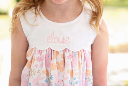 Child wearing a white top with 'elise' embroidered on it and a floral dress.