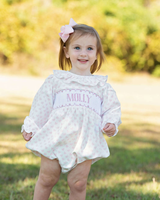 Child wearing a white valentine bubble with 'MOLLY' embroidered on it, standing outdoors.
