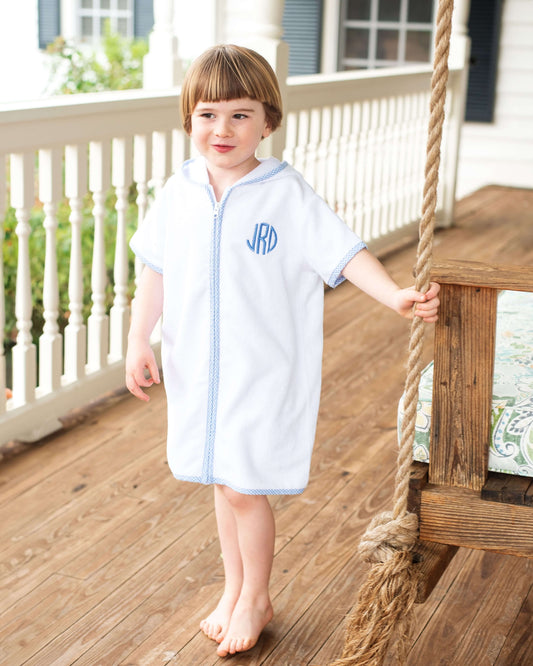 Child wearing a white zip-up cover-up with blue trim on a wooden porch.