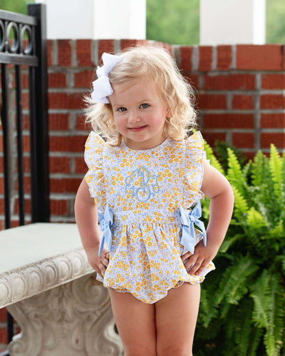 Child wearing a yellow floral bubble with blue accents outdoors.