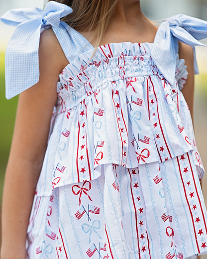 Child wearing an outfit with red, white, and blue patterns and bow straps.