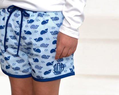 Child wearing blue shorts with whale pattern on a plain background