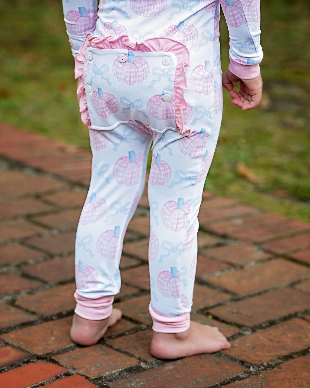 Child wearing light blue and pink pajama pants with pumpkin and pink cuffs and ruffles on a brick path.