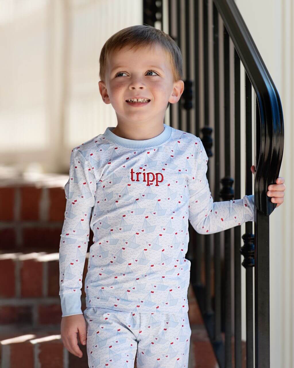 Child wearing light blue pajamas with 'tripp' embroidered on them, standing outdoors.