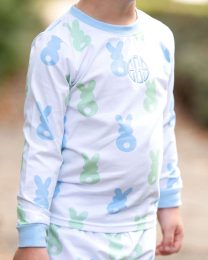Child wearing pajamas with blue and green animal prints and a monogram on a blurred outdoor background