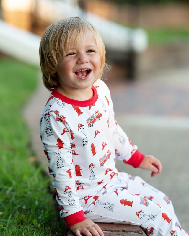 Child wearing pajamas with fire truck pattern sitting on grass