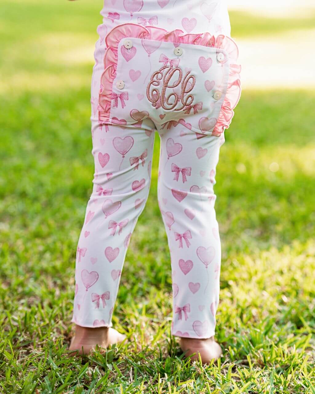 Child wearing pink and white zipper pajamas with heart and bow patterns on grass.