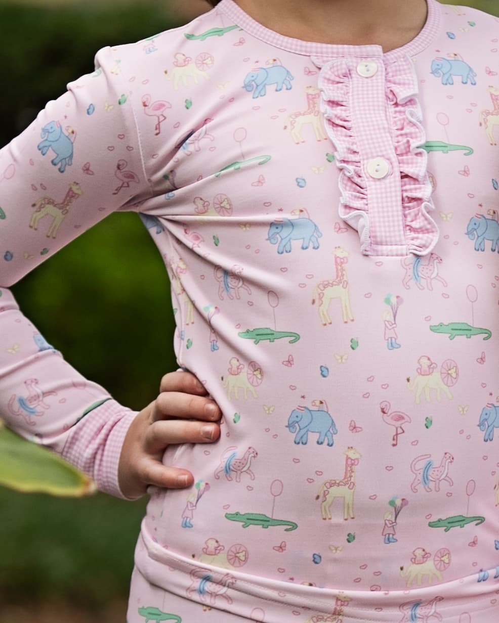 Child wearing pink long-sleeve pajamas with animal birthday prints against a green background
