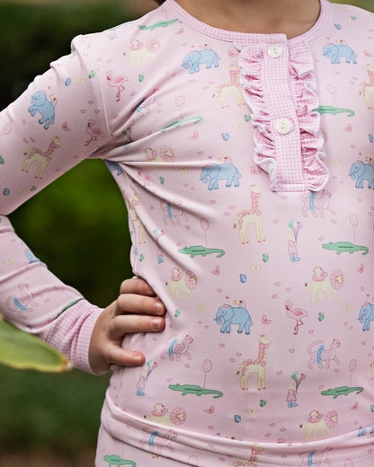Child wearing pink long-sleeve pajamas with animal birthday prints against a green background