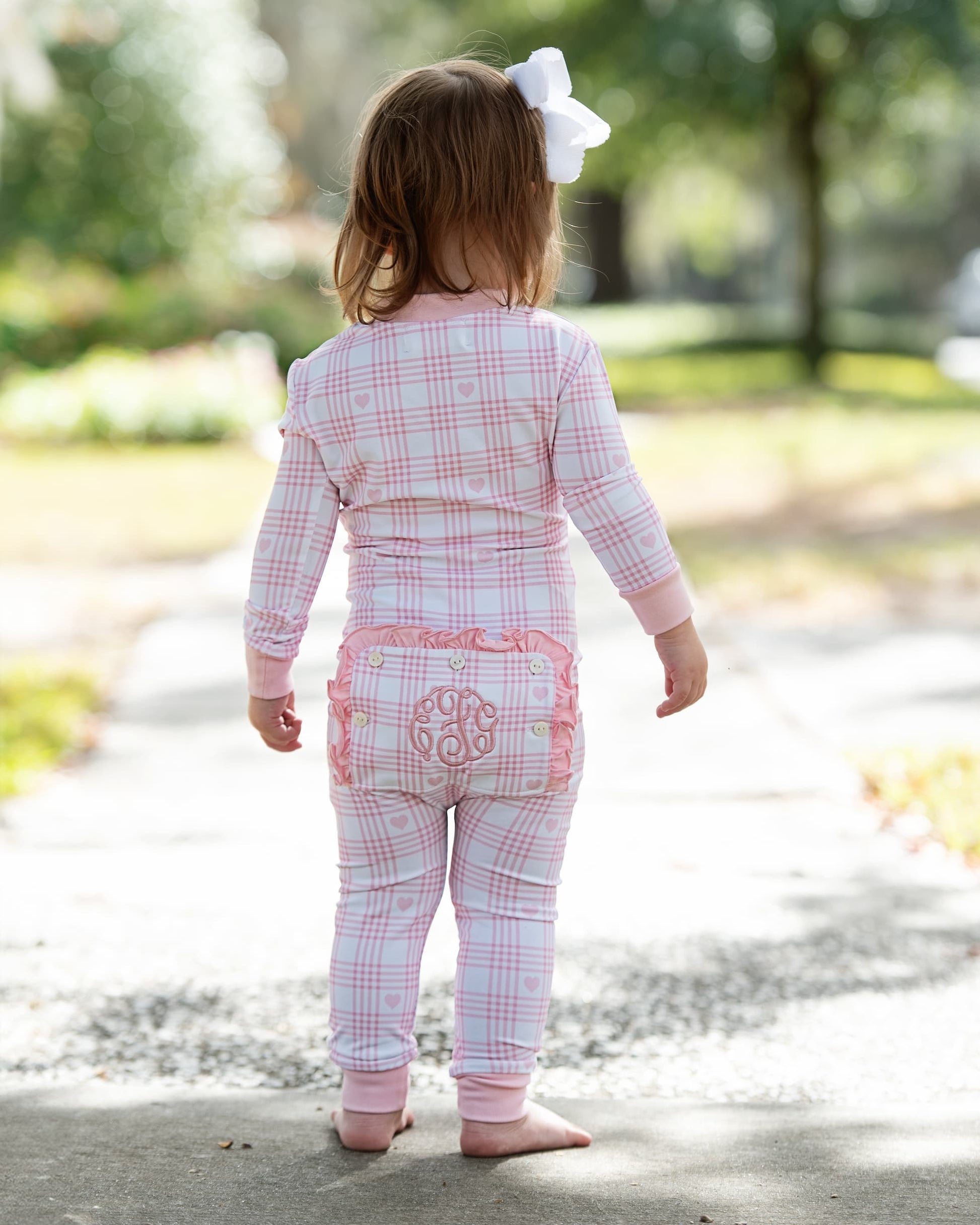 Child wearing pink plaid pajamas with a white bow in a park setting