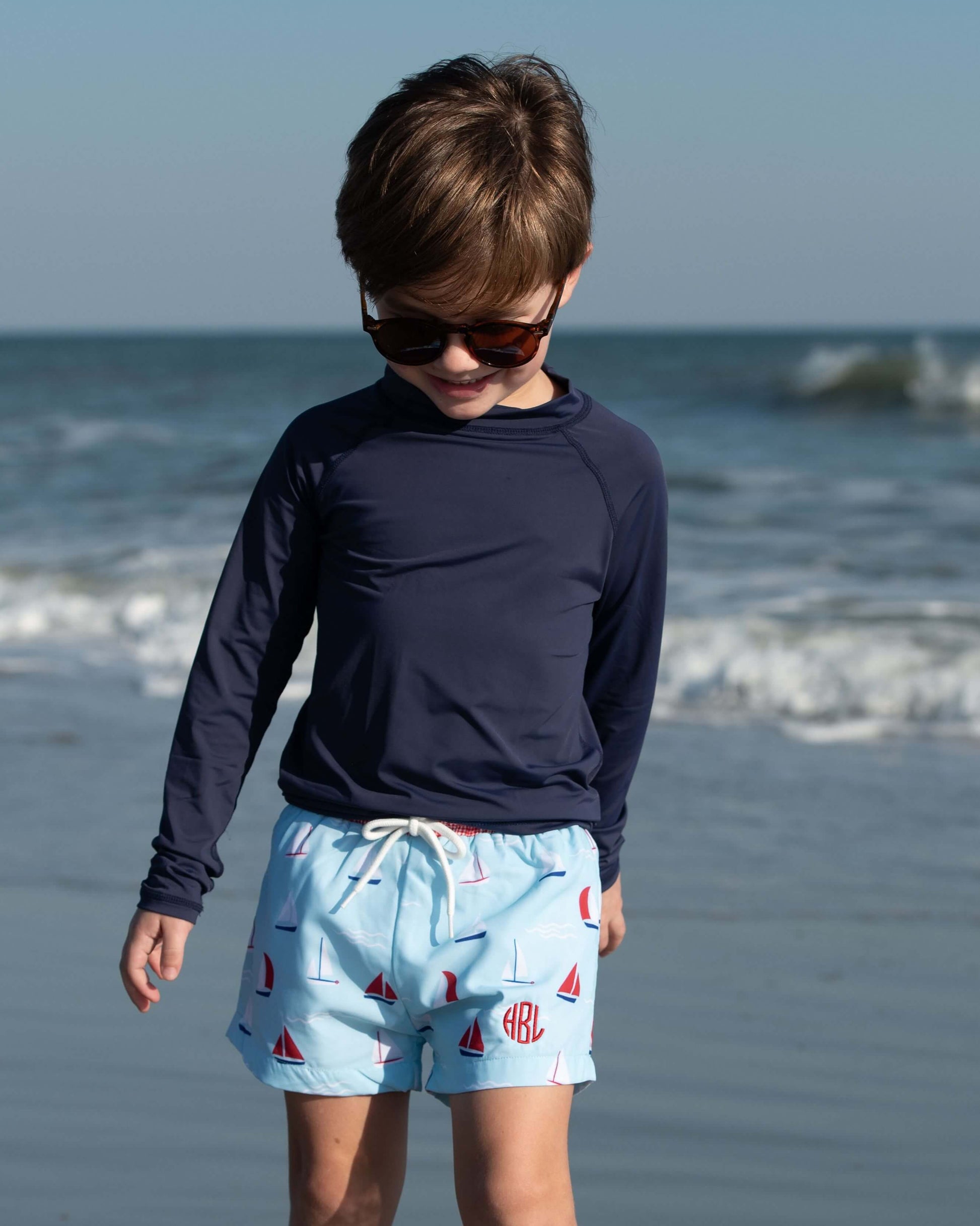 Child wearing sunglasses and swim shorts on a beach