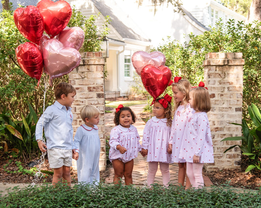 Children holding heart-shaped balloons in a garden setting