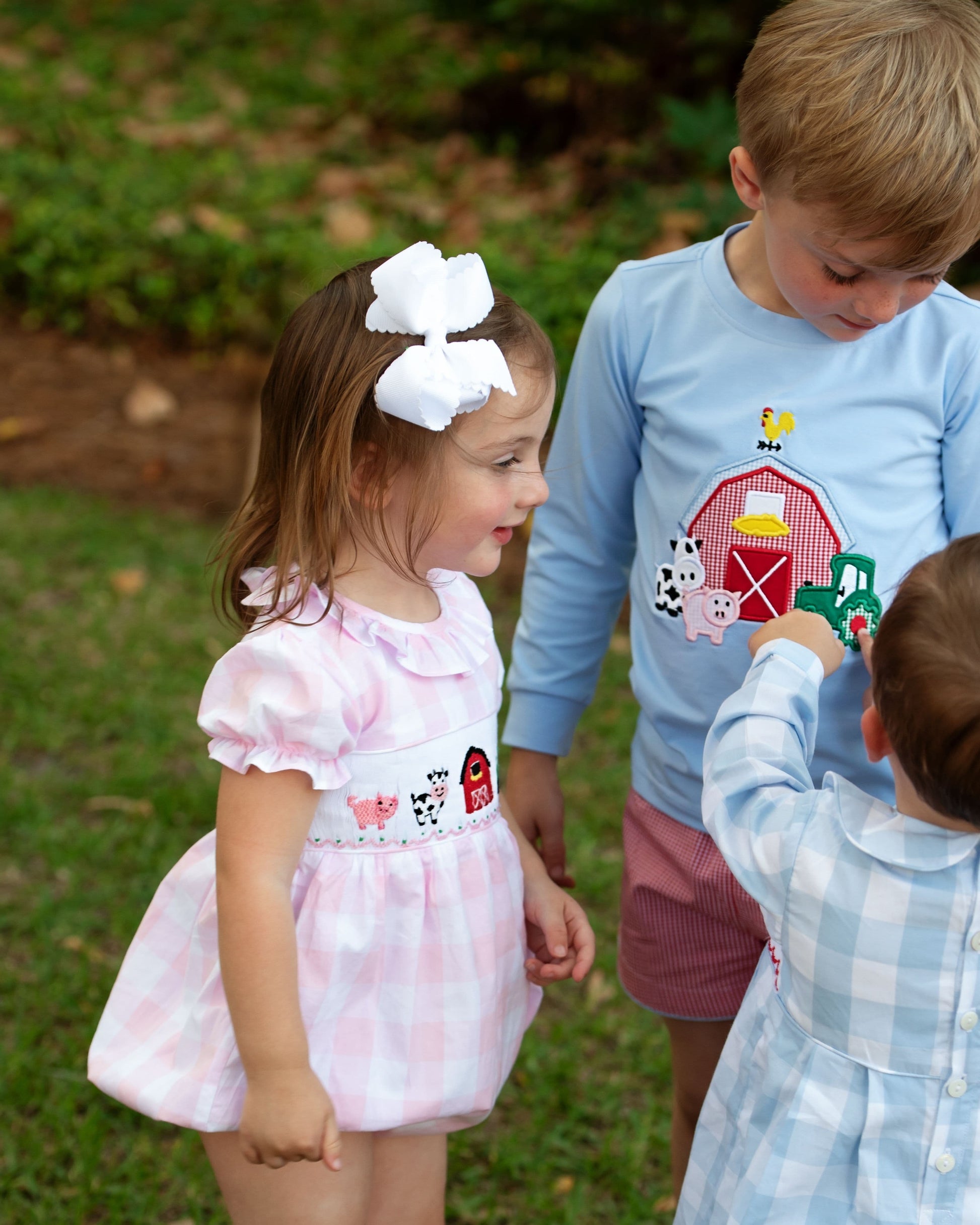 Children playing outdoors with a focus on a young girl in a pink dress with farm-themed design.