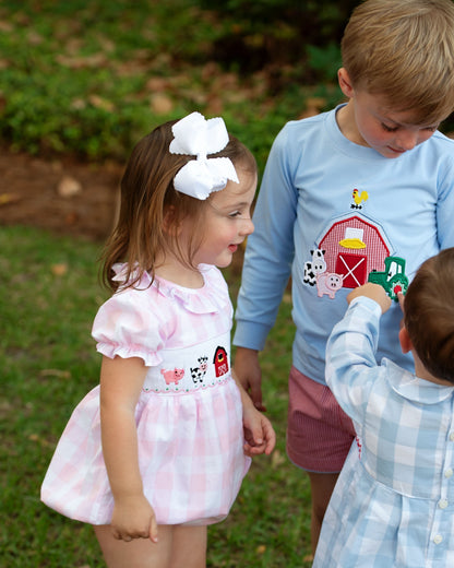 Children playing outdoors with a focus on a young girl in a pink dress with farm-themed design.
