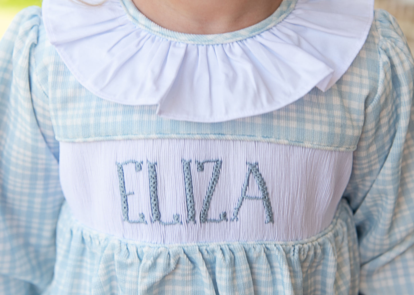 Children's dress with 'Eliza' embroidered on the chest, featuring a blue and white checkered pattern.