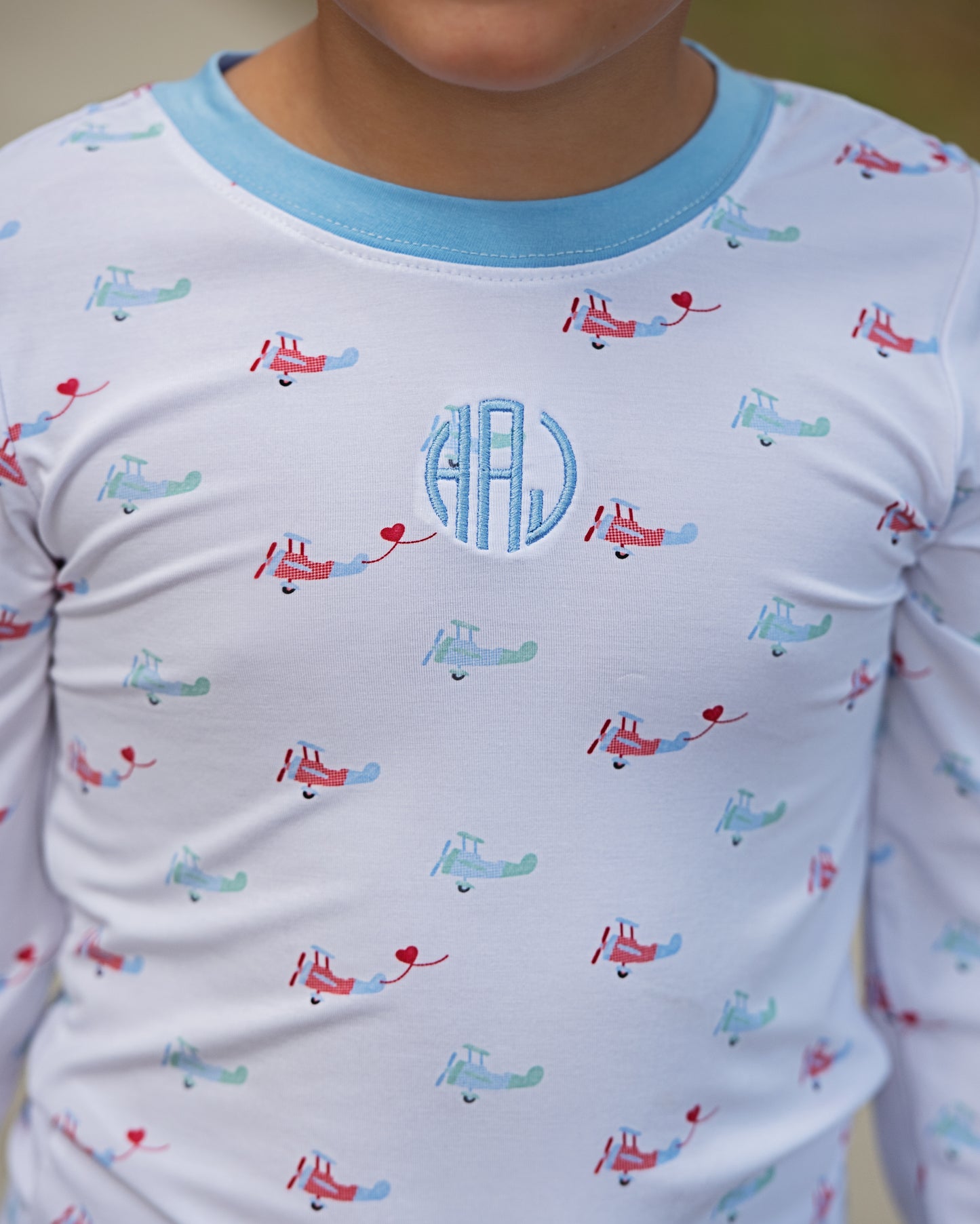 Children's long-sleeve pajama set with airplane pattern and monogram on a plain background
