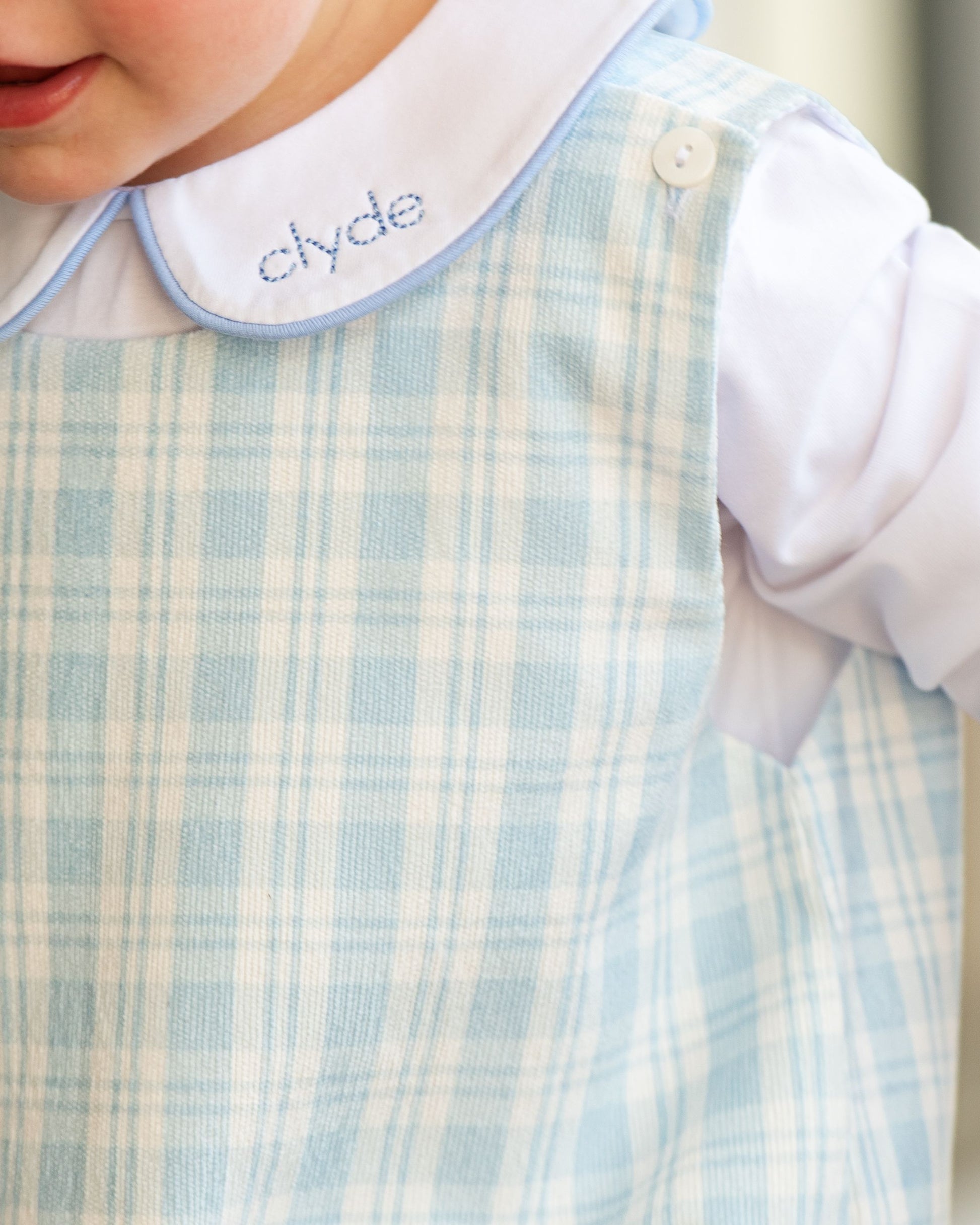 Close-up of a baby's outfit with a checkered bib and shirt, featuring the name 'clyde'.