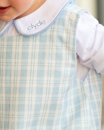 Close-up of a baby's outfit with a checkered bib and shirt, featuring the name 'clyde'.