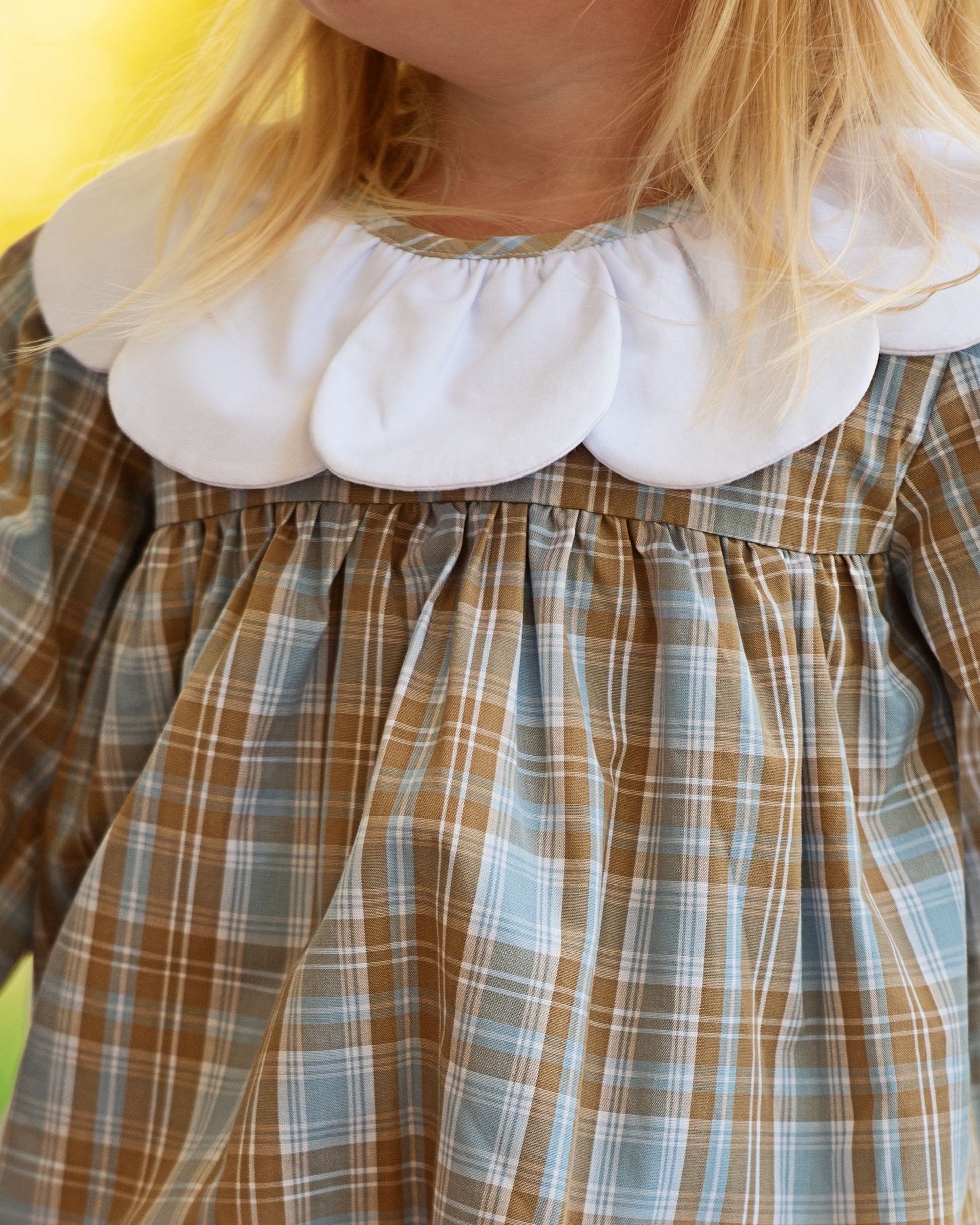 Close-up of a child's dress with a white ruffled collar and plaid pattern.